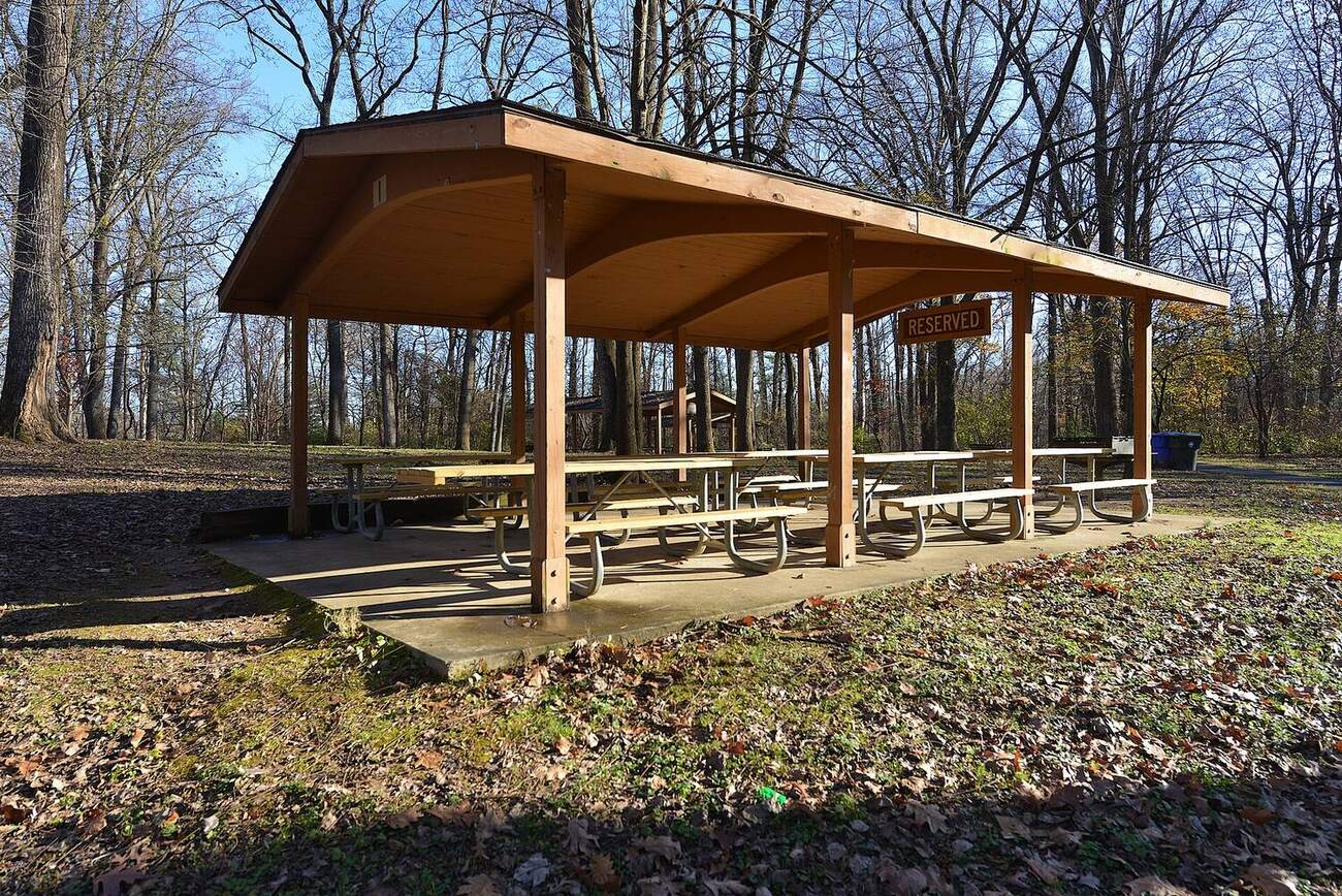 A timber picnic pavilion with rows of picnic tables and a Reserved sign hanging from the beam.
