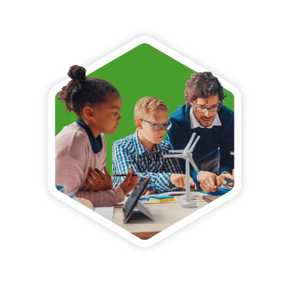 GREEN Charter teacher and two students examining a small model wind turbine and a tablet together in a classroom, learning renewable energy