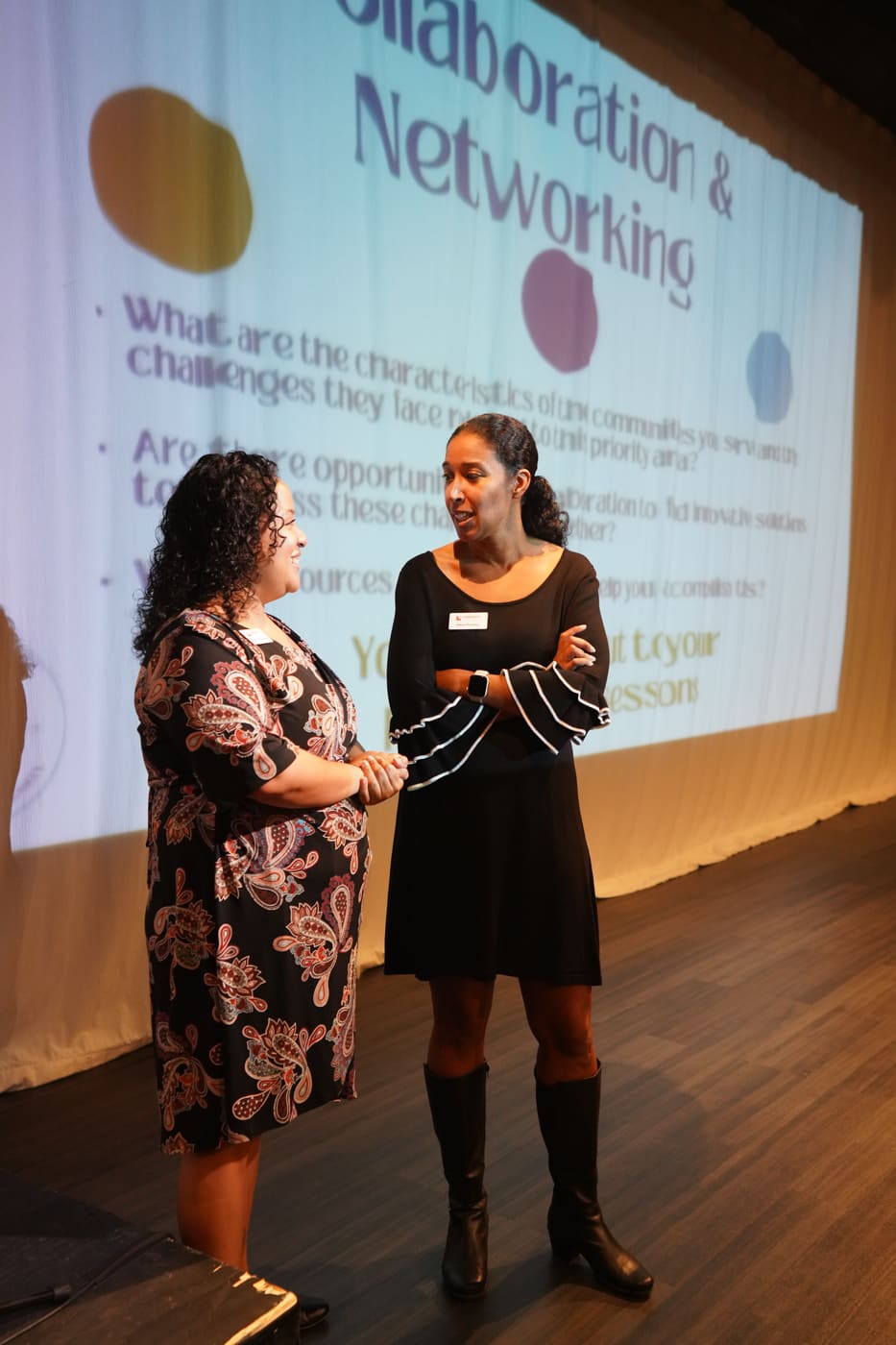 Two women talking at the stage beside the Collaboration and Networking screen