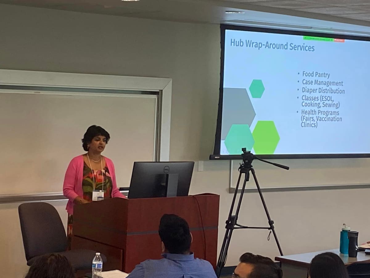 A presenter beside the "Hub Wrap-Around Services" slide at the Community Navigation Summit