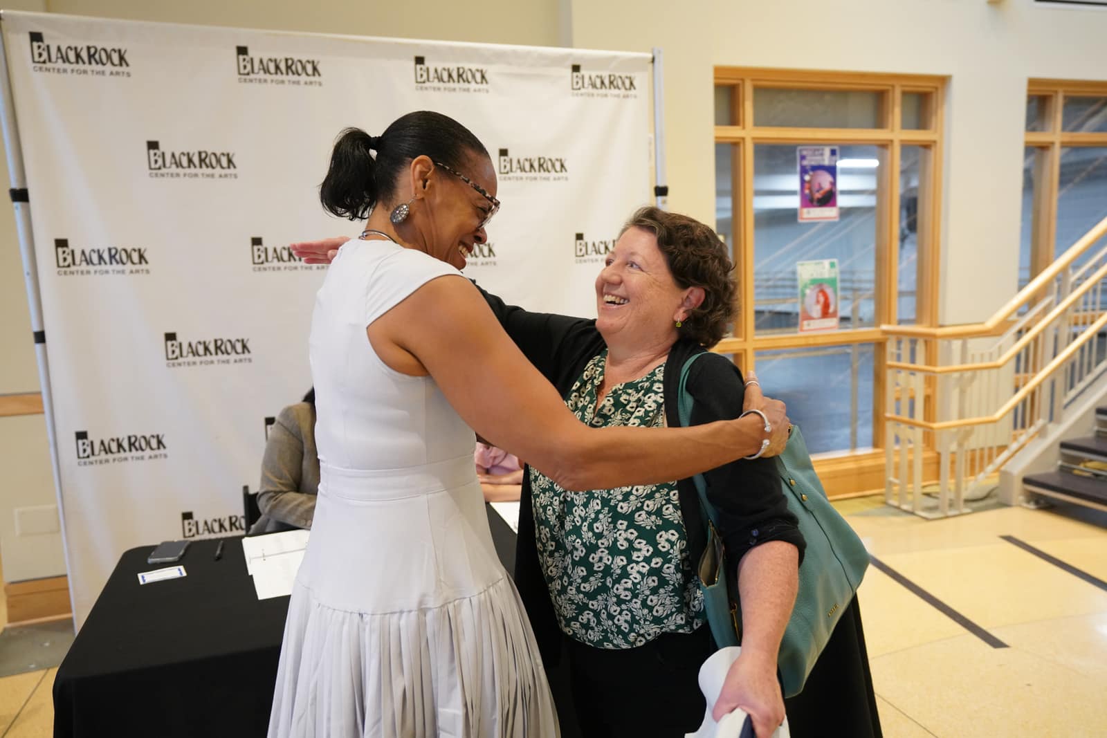 Two women embracing in front of the BlackRock Center for the Arts backdrop at HIF's 50th Anniversary breakfast