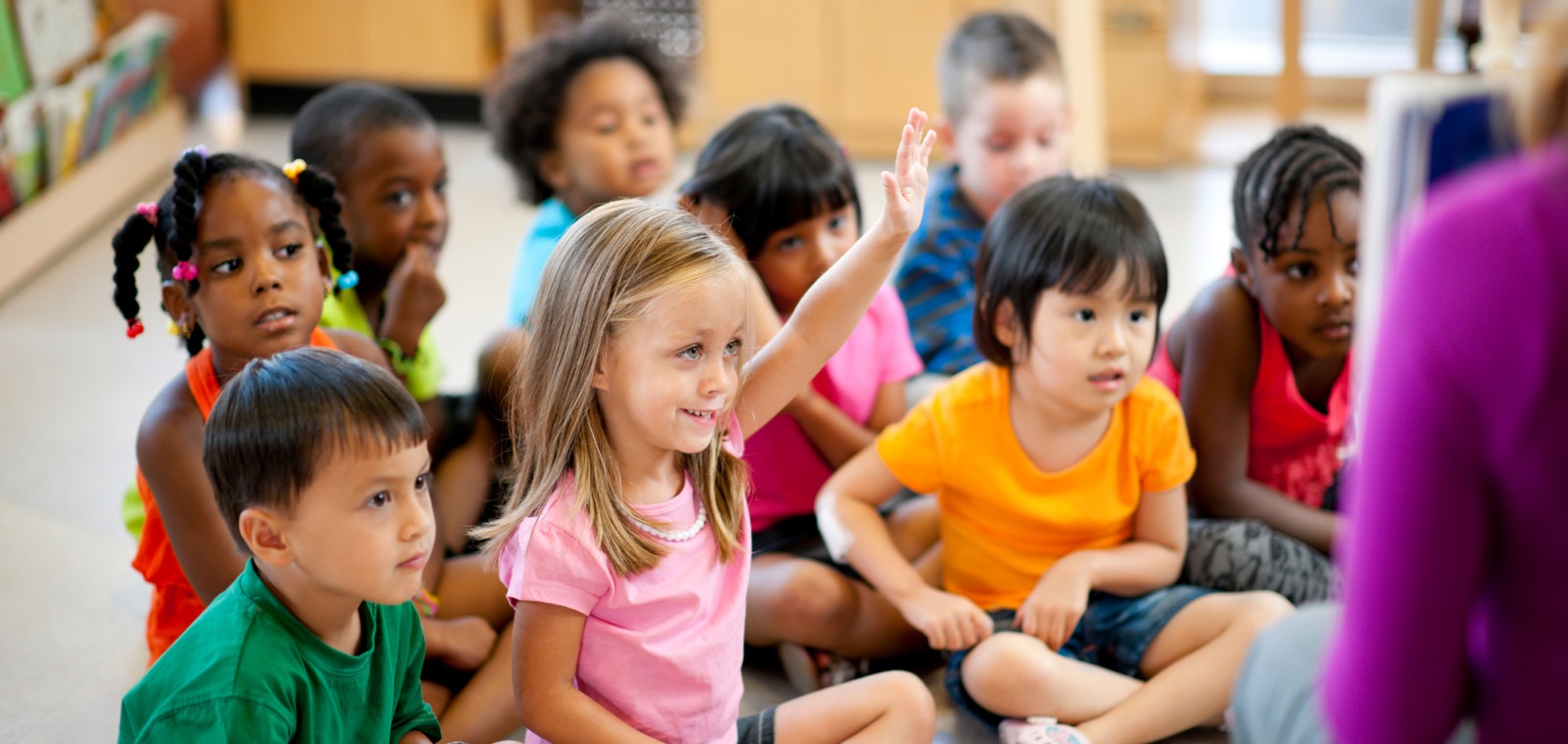 A group of preschool children raising their hands during a classroom activity