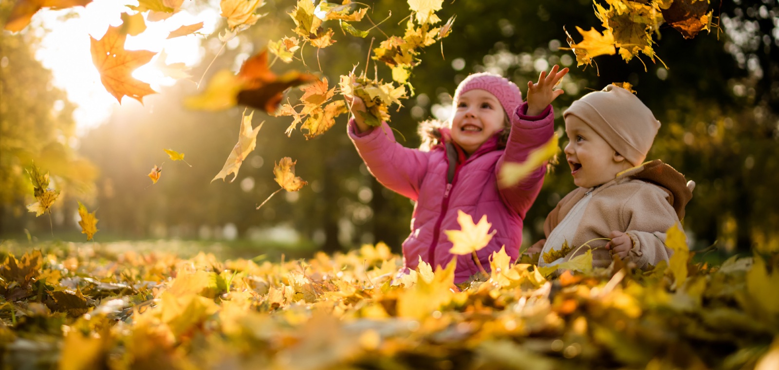 Two young children throwing autumn leaves into the air