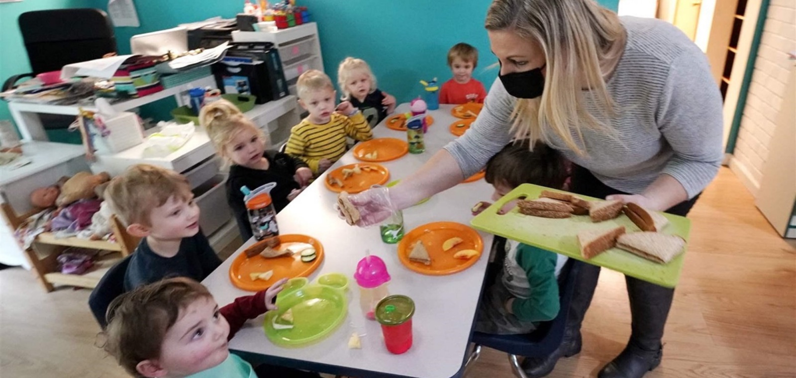 A child care provider serving lunch to a table of preschoolers