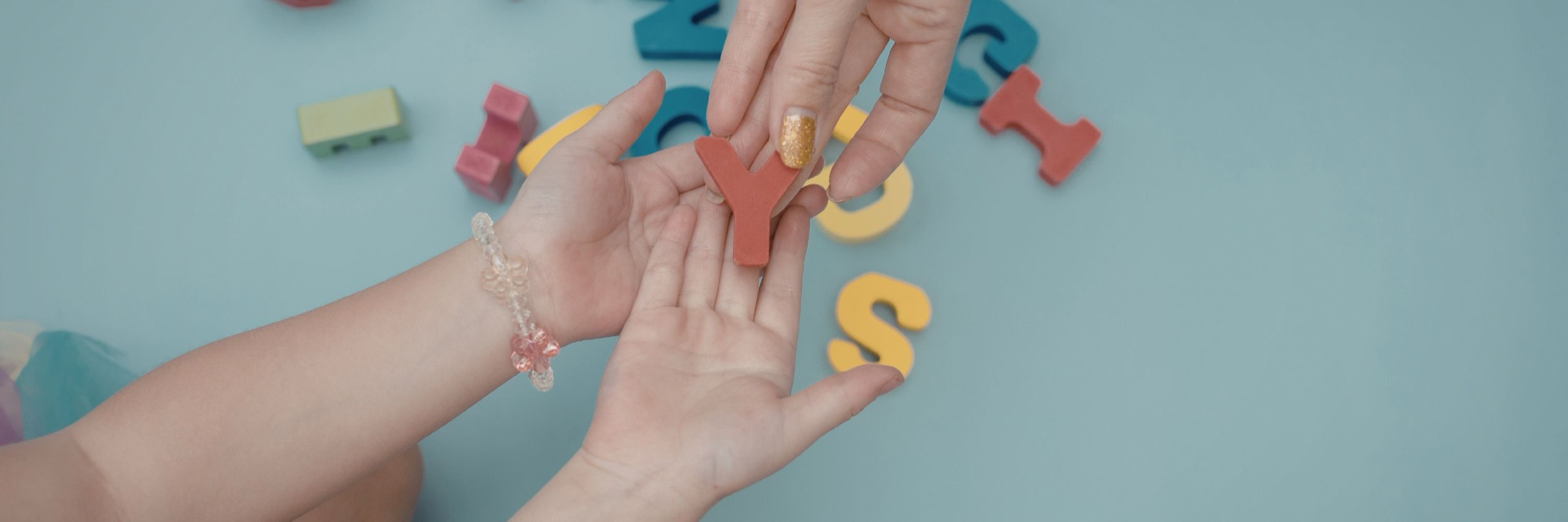 An adult hand passing a foam letter to a small hand during a learning activity
