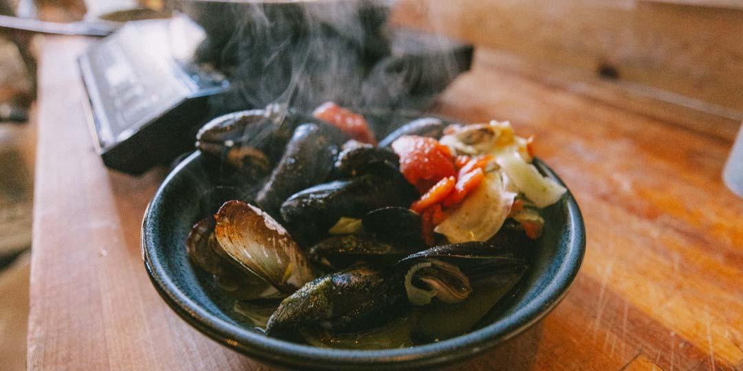 A steaming bowl of Penn Cove mussels on a wooden table