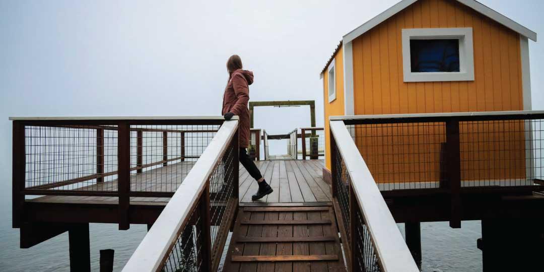 A guest walking the Captain Whidbey Inn's dock past its yellow boathouse on Penn Cove