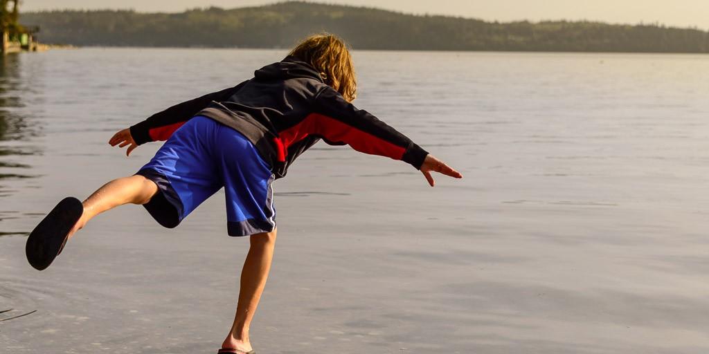 A boy mid-leap off a driftwood log at the water's edge on Camano Island
