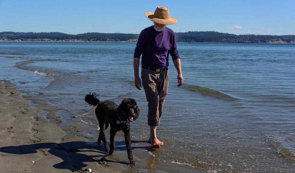 A man and his dog walking the waterline at Double Bluff Beach, tide out and Useless Bay flat behind them