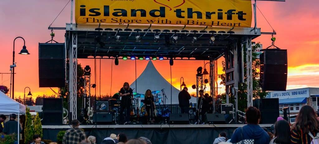 An audience on the lawn at dusk before the lit Island Thrift stage at Windjammer Park