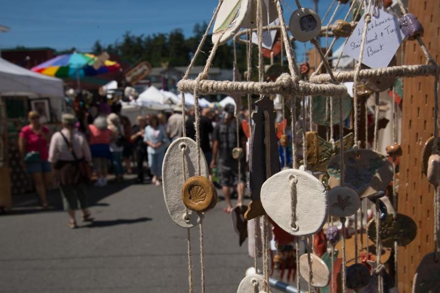 Driftwood mobiles hanging at a Coupeville festival booth, browsers filling the street behind