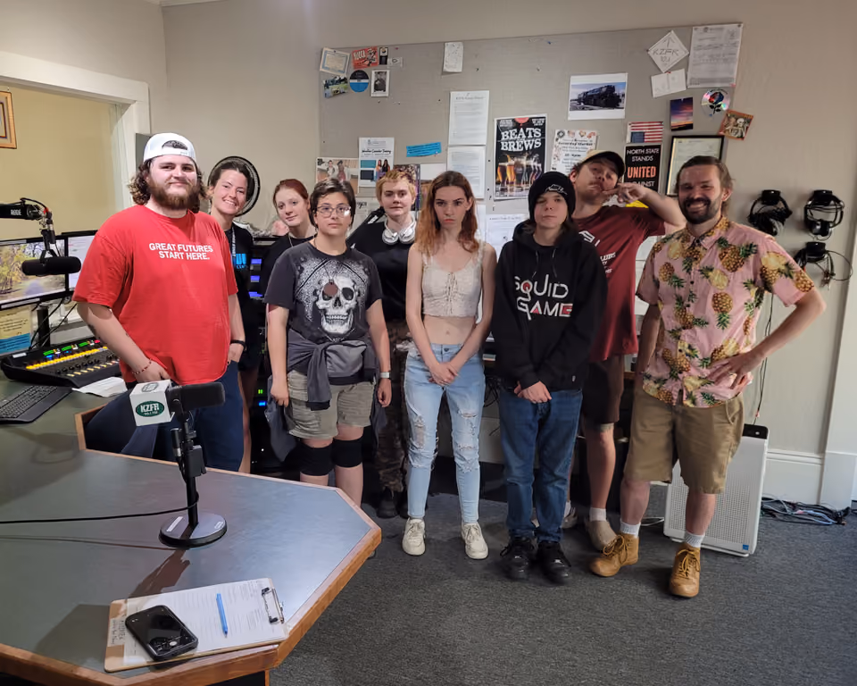 Nine young visitors and staff from the Boys & Girls Club pose together in the KZFR studio beside the mixing board and a microphone