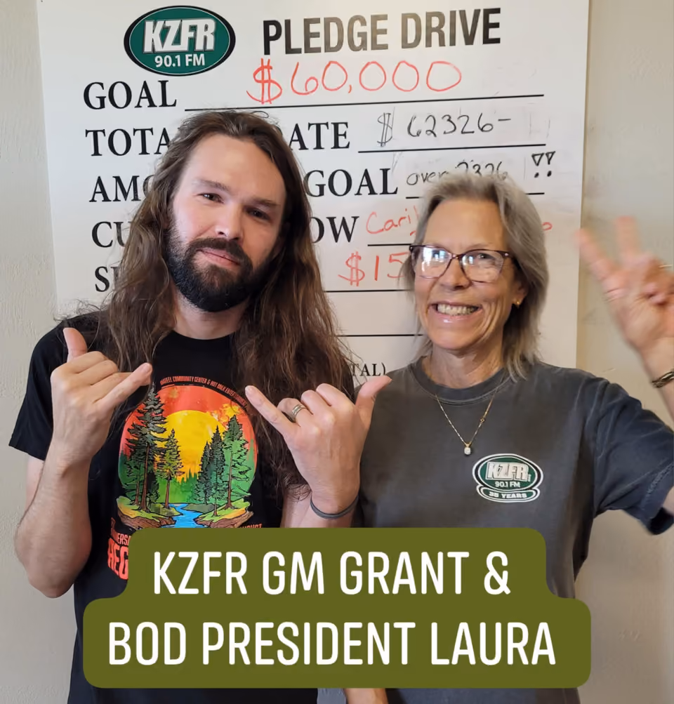 KZFR GM Grant and board president Laura smiling and making hand gestures in front of a Pledge Drive board showing a $60,000 goal and $62,326 raised