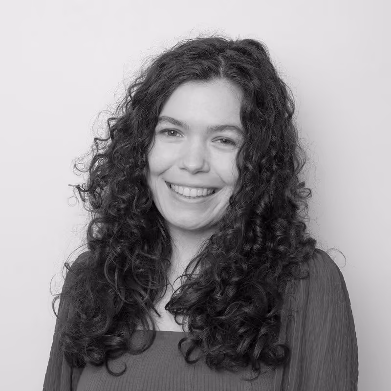 Black and white portrait of a smiling woman with long, curly dark hair, wearing a pleated