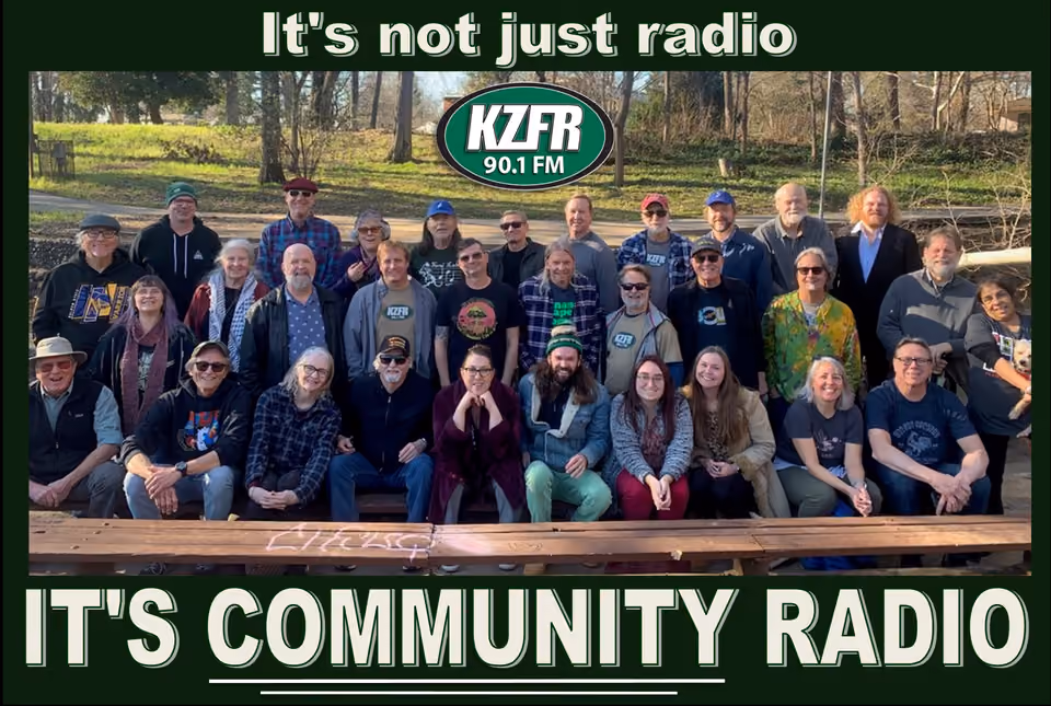 Group photo of about thirty KZFR volunteers posed outdoors on and behind a wooden bench, with the KZFR 90.1 FM logo and the words "It's community radio"