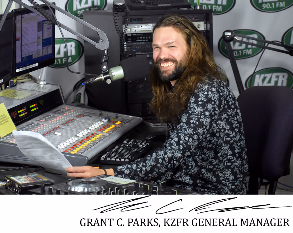 Grant C. Parks, KZFR General Manager, smiling at the on-air studio mixing board and microphone, with a signature beneath