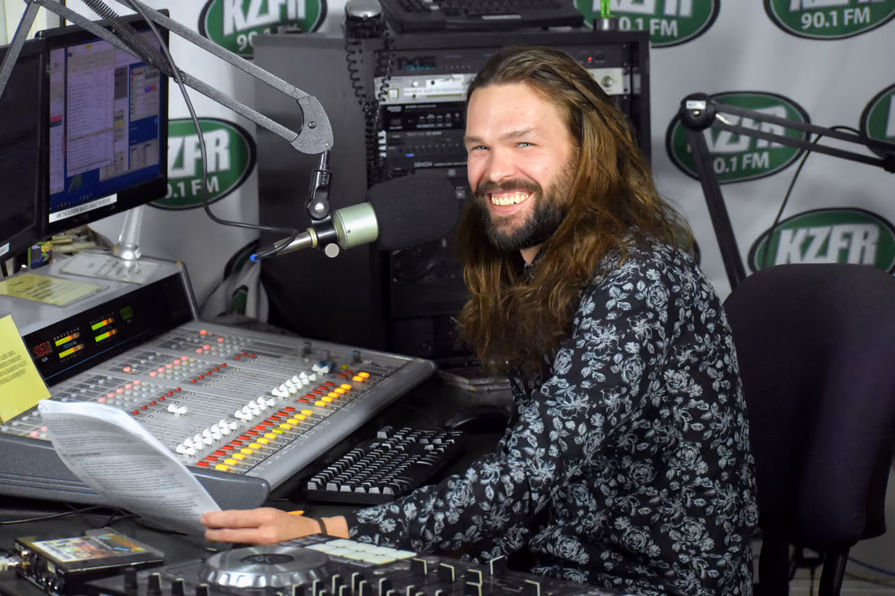 Grant C. Parks, general manager, smiling at the mixing board in the KZFR studio, holding a sheet of paper