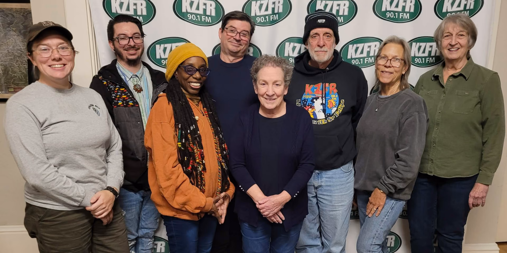 Members of KZFR's 2025-2026 Board of Directors standing together in front of the station backdrop.