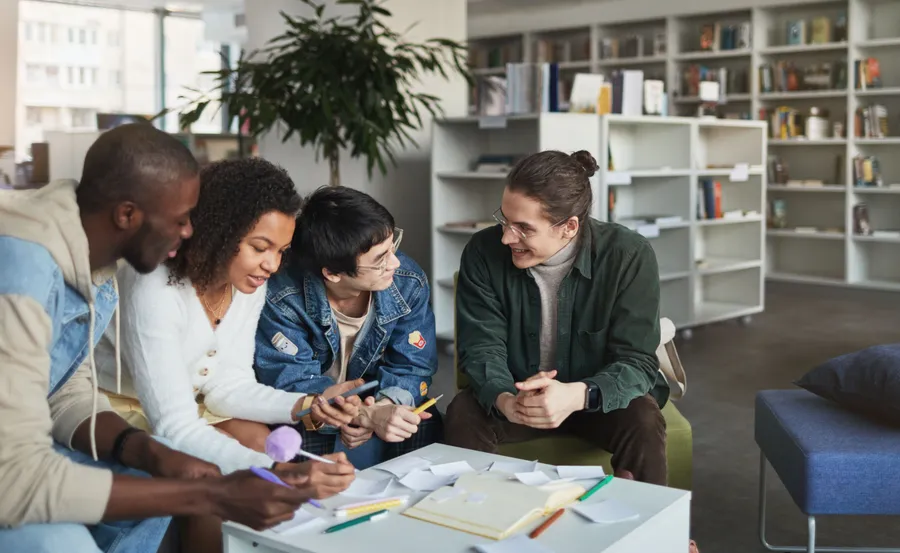 Four students smiling and working through notes together around a library table.