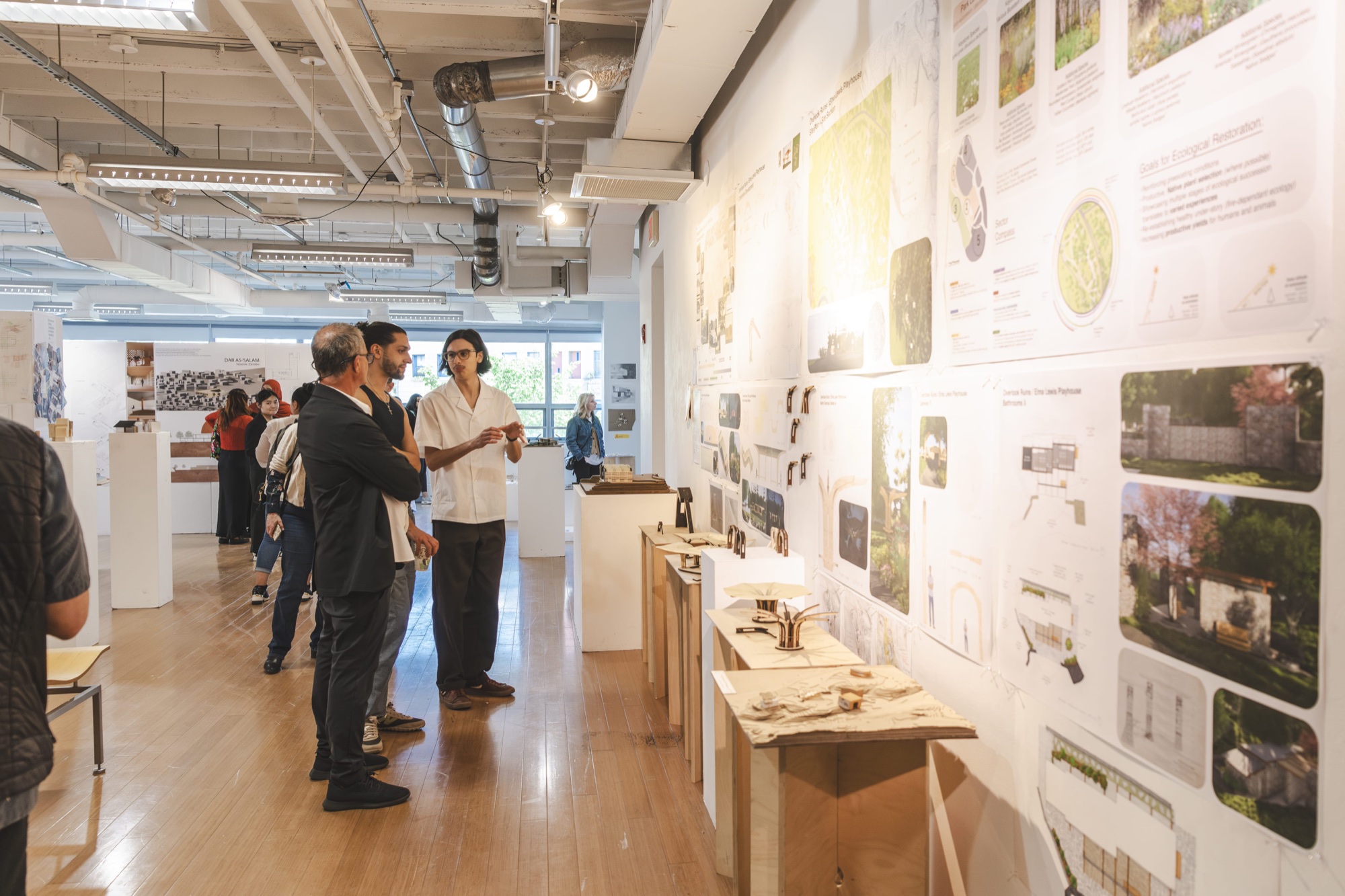 People view architectural models and design boards on a gallery wall at MassArt.