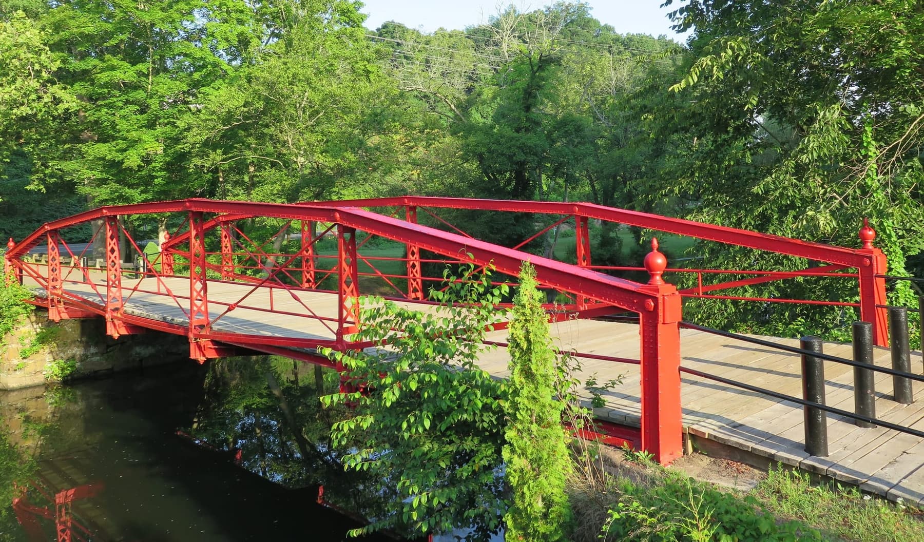 The historic red metal bridge crossing a wooded stream in spring.