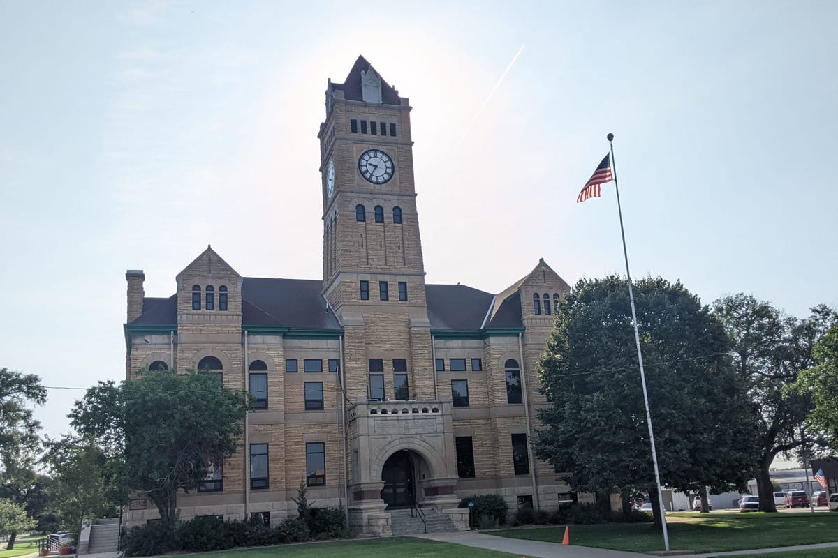The Mitchell County Courthouse in Beloit, native limestone with its clock and bell tower, under a blue sky