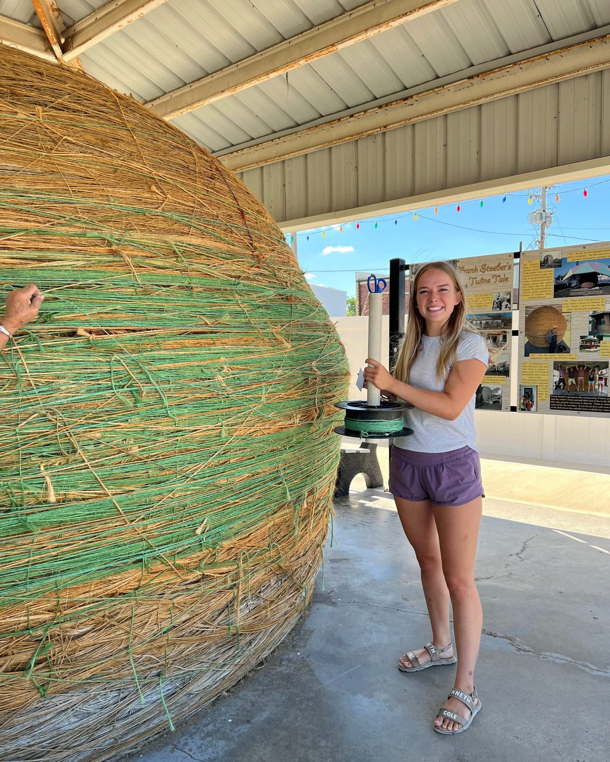 A visitor with a hand on the World's Largest Ball of Twine under its gazebo