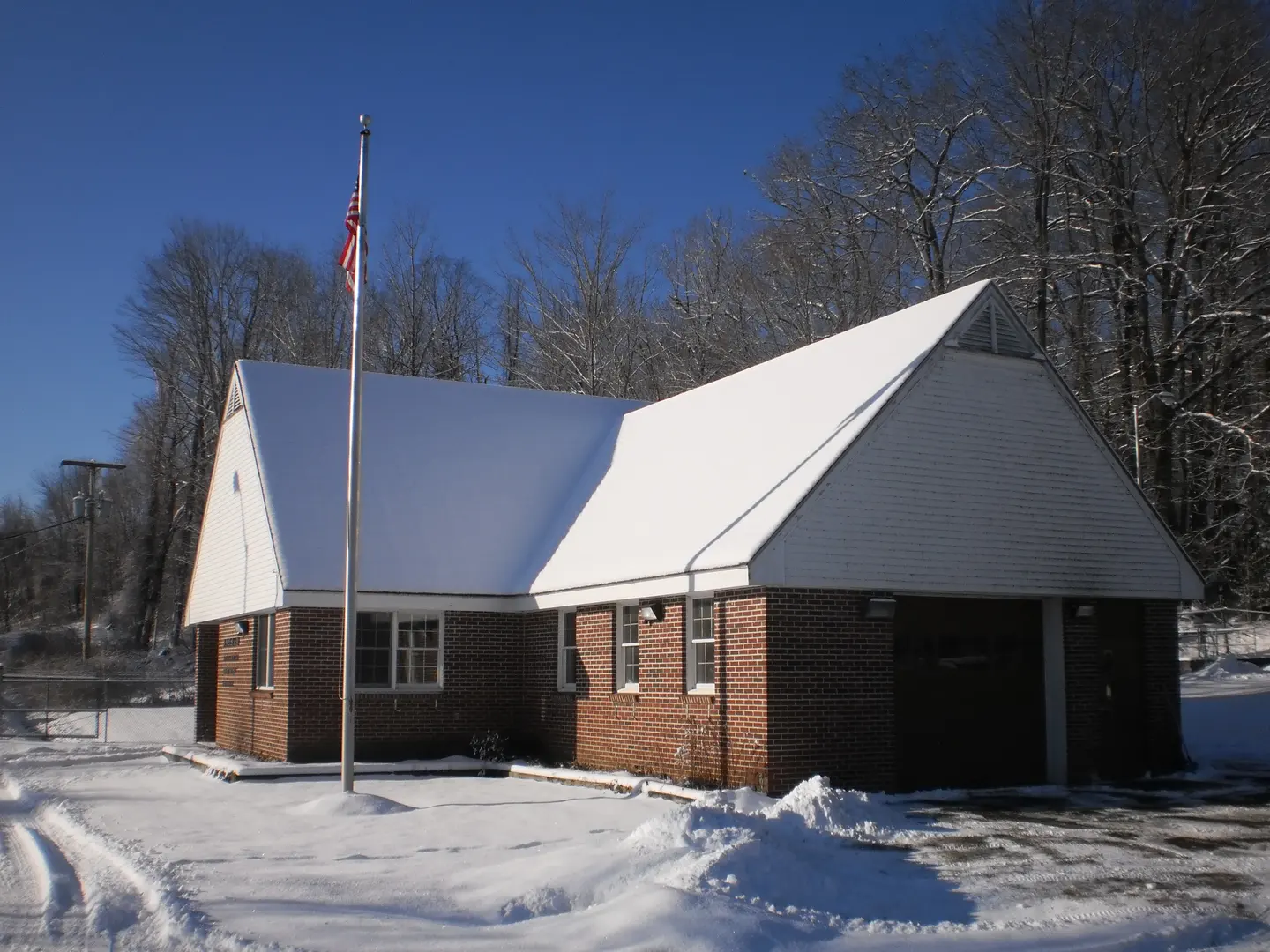 A small white-roofed treatment facility building with a flagpole, in snow