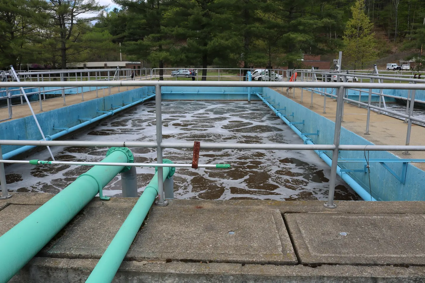 Turquoise aeration tanks with green pipes at a wastewater treatment facility