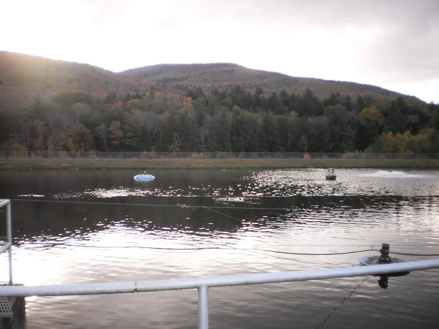 A wastewater lagoon with floating aerators and wooded mountains behind it