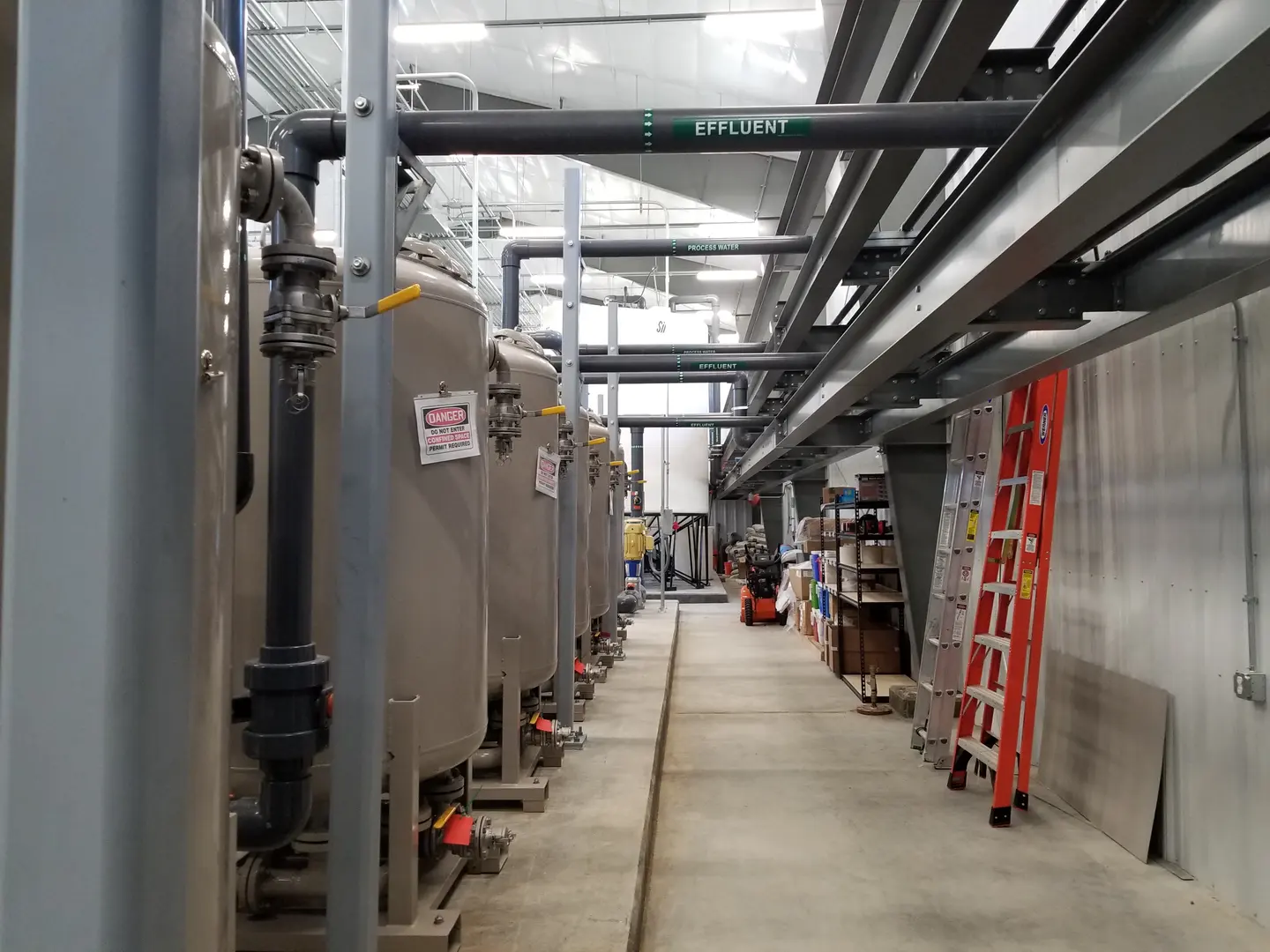 A long aisle of treatment vessels and overhead piping inside a building