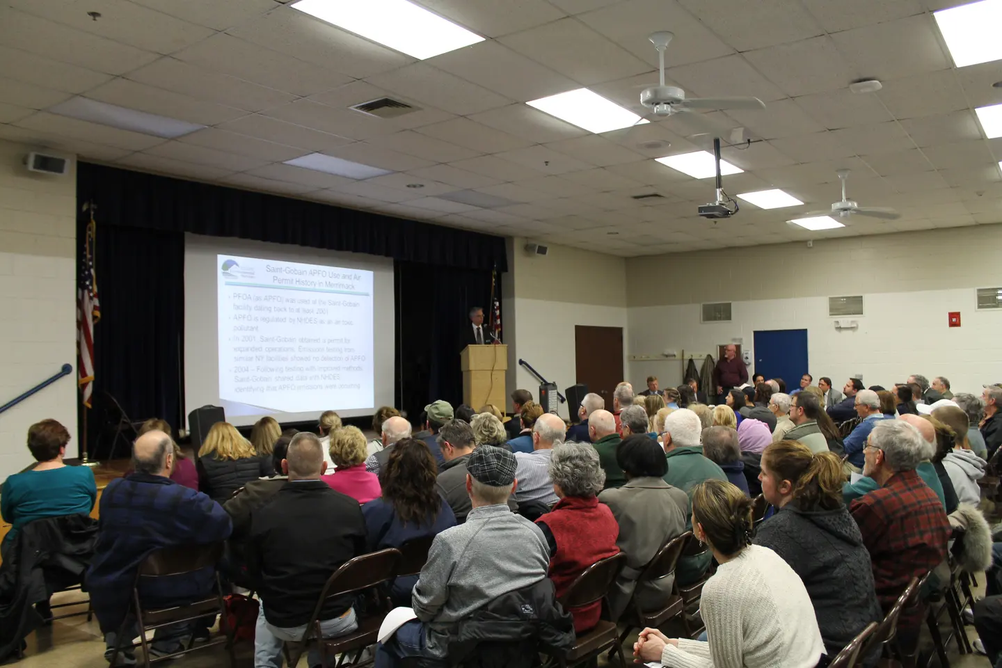 A speaker at the front of a full hall with a projected slide behind him