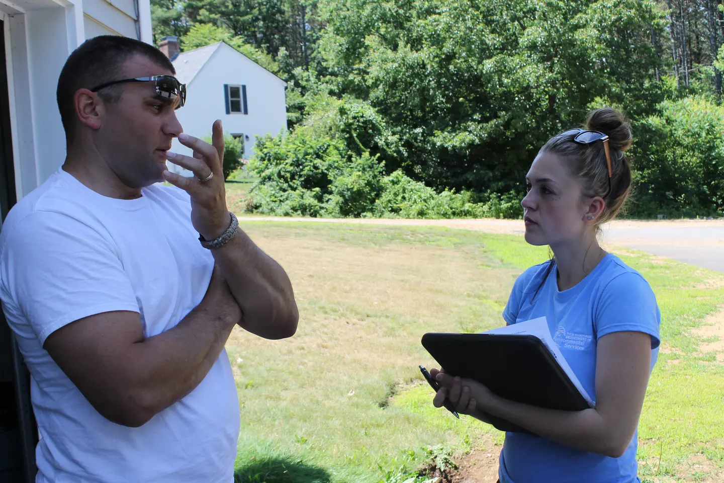A man talks with a woman holding a clipboard outside a house