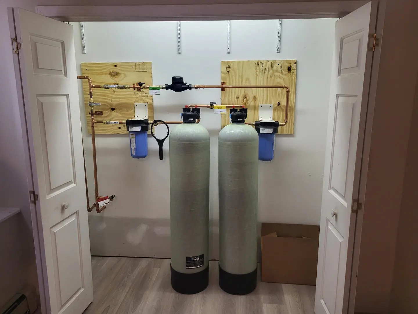 Two filter tanks and blue cartridge housings mounted on a basement wall