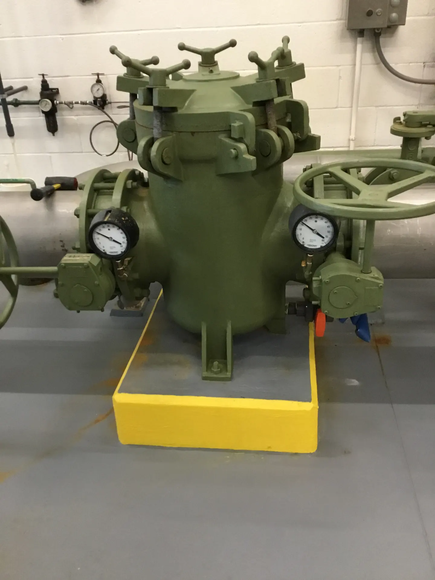 A green strainer housing with pressure gauges and handwheel valves