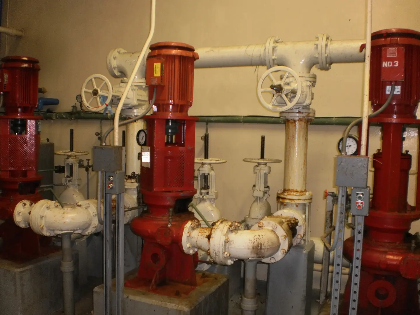 Red pumps and white pipes with valves in a pump room