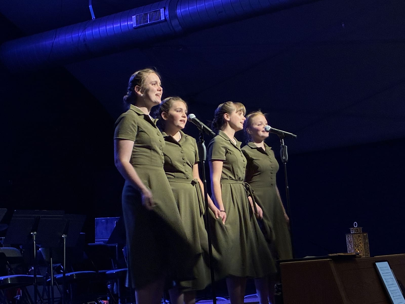 Four singers in green dresses at the microphones in a Lamp Post Creative Learning Center show