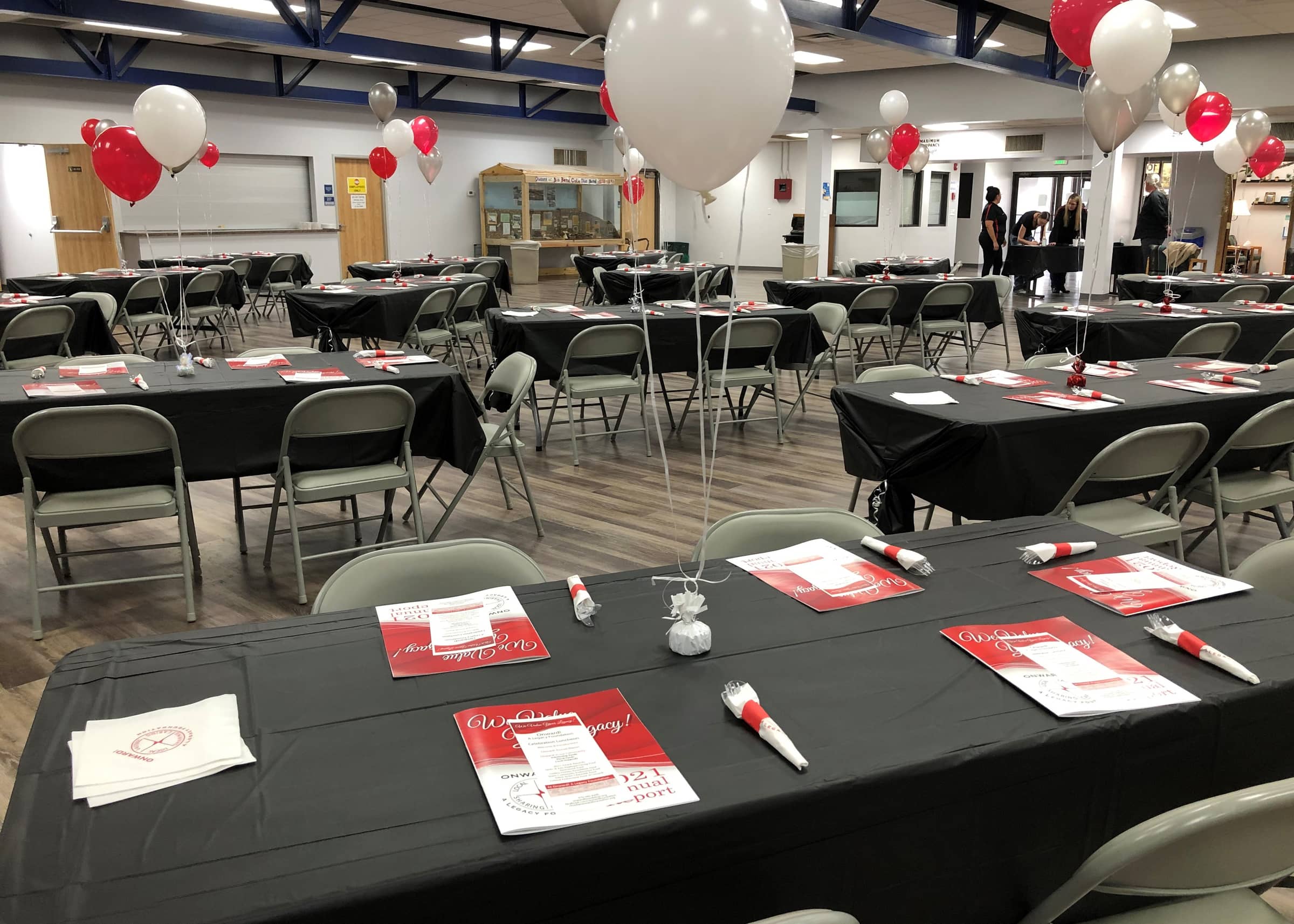 The Celebration Luncheon room set with black tablecloths, red programs, and red, white, and silver balloons