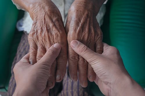 A younger person’s hands holding an elder’s hands