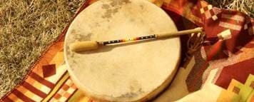 A hand drum and beater resting on a woven blanket