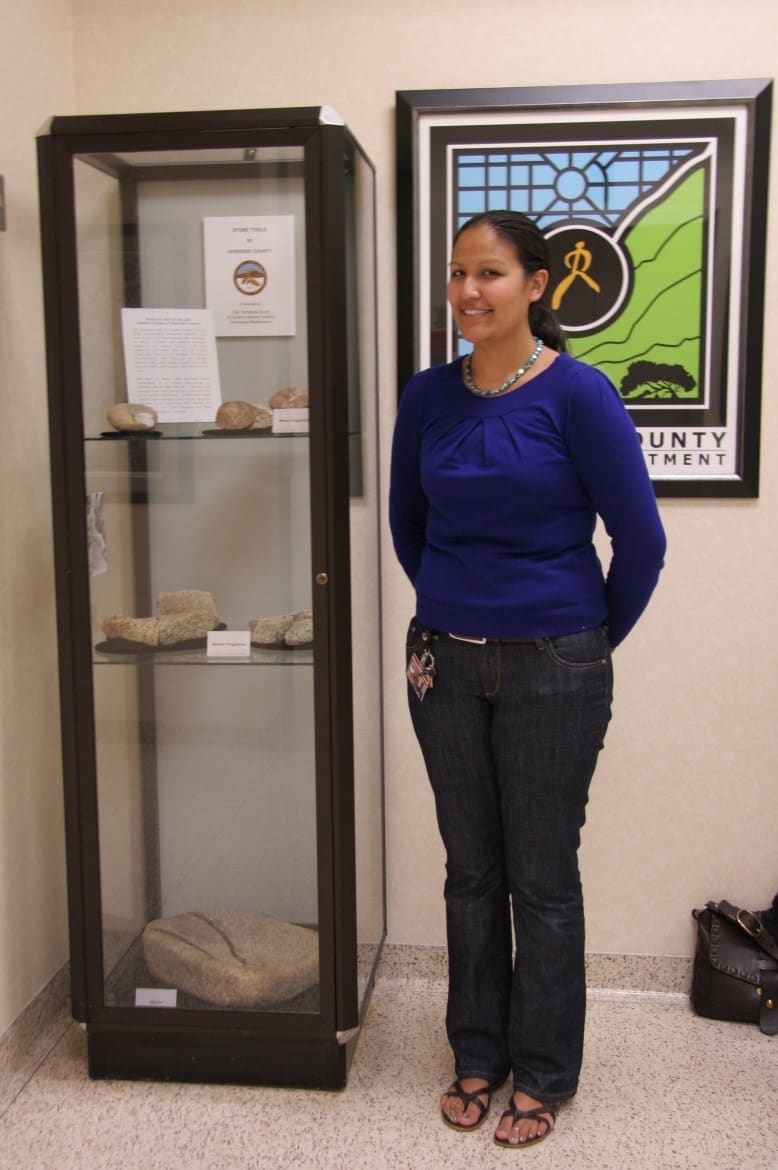A staff member beside a display case and a stained-glass panel in the exhibit room
