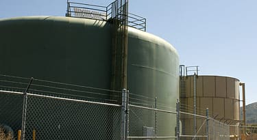 Green water storage tanks behind a chain-link fence