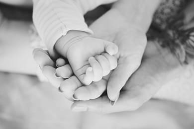 A baby’s hand held in an adult’s hands, in black and white