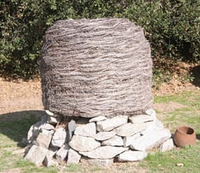A traditional acorn granary of woven willow, raised on stones beneath an oak