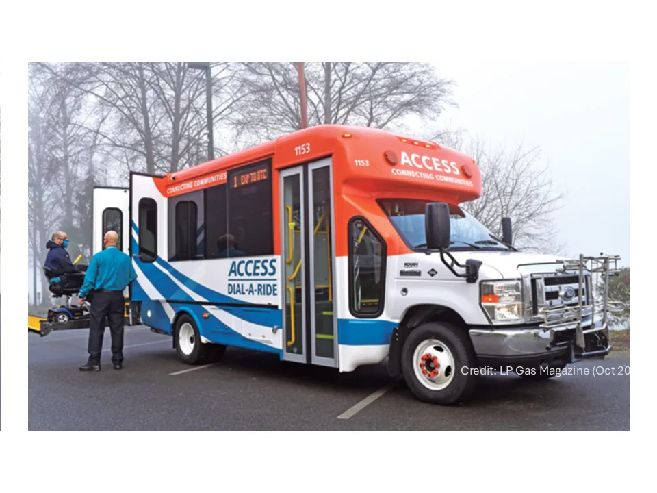 A rider in a wheelchair on the lift of an ACCESS Dial-a-Ride bus, with the driver beside it.