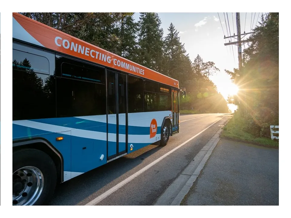 Kitsap Transit bus marked Connecting Communities on a tree-lined road at sunrise.