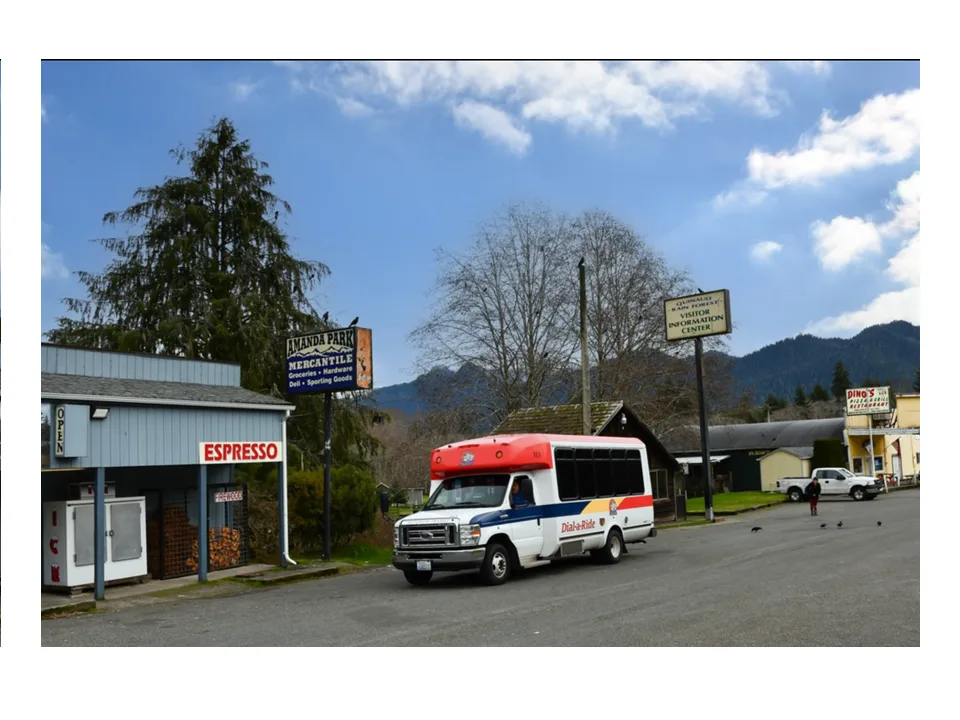 A Dial-a-Ride minibus parked outside the Amanda Park Mercantile, with forested hills behind.