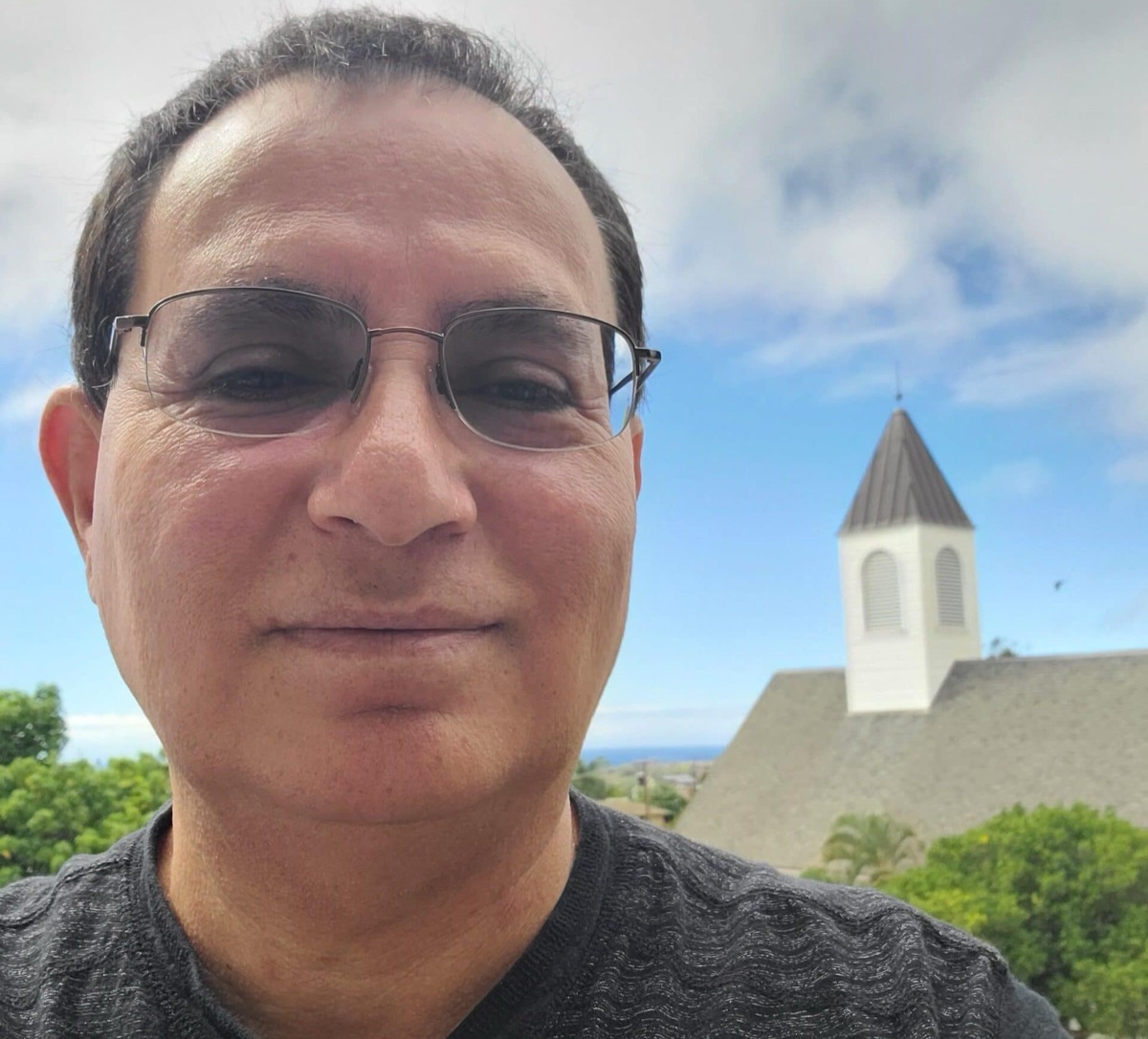 A PSR alum smiling outdoors with the Chapel of the Great Commission steeple behind him