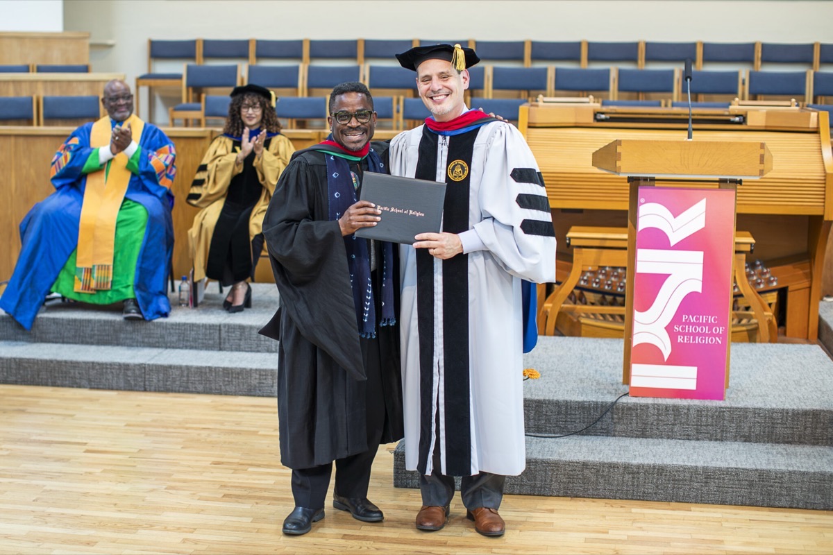 A graduate receives their diploma on stage in front of the PSR podium banner