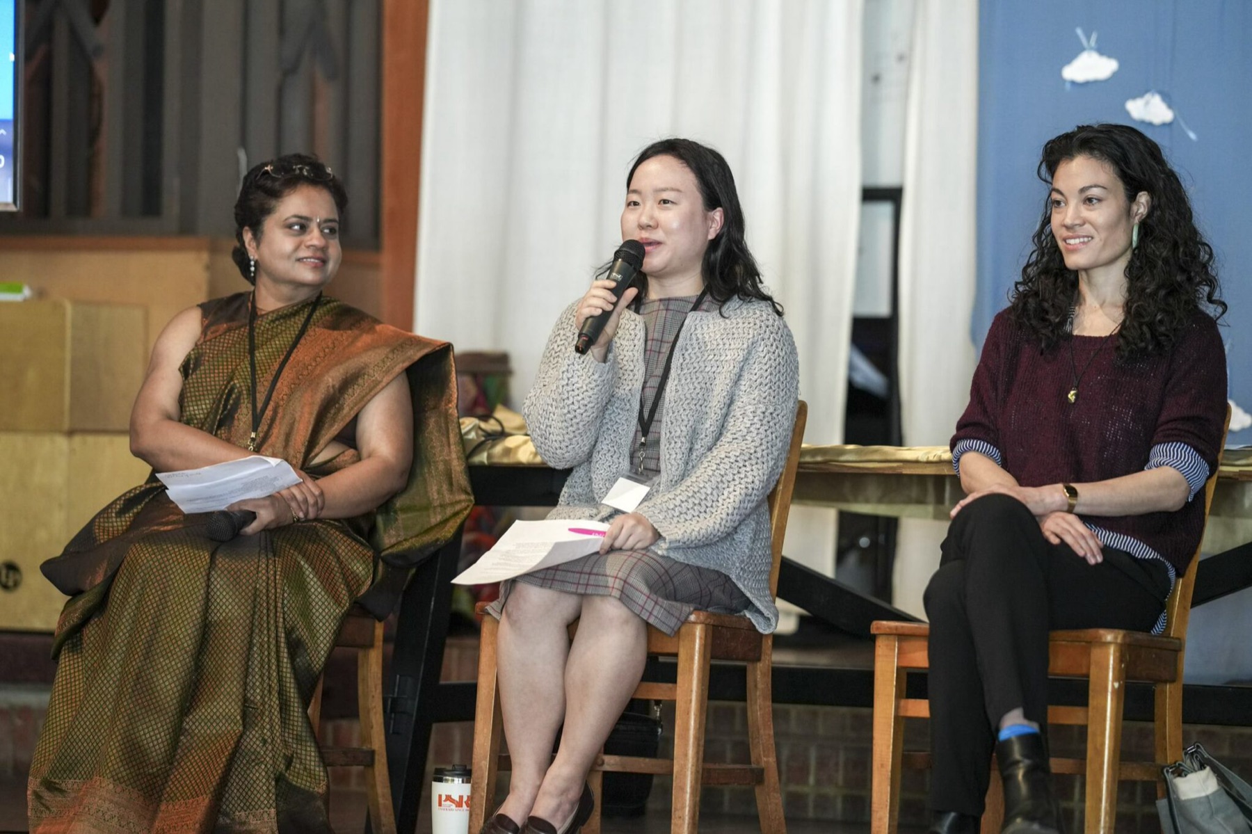 Three panelists in conversation, with the center speaker holding a microphone